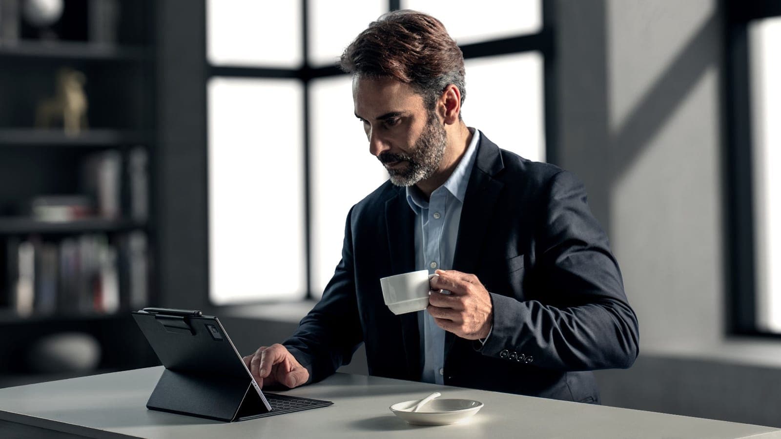 A professional working on a BOOX tablet with keyboard case over coffee