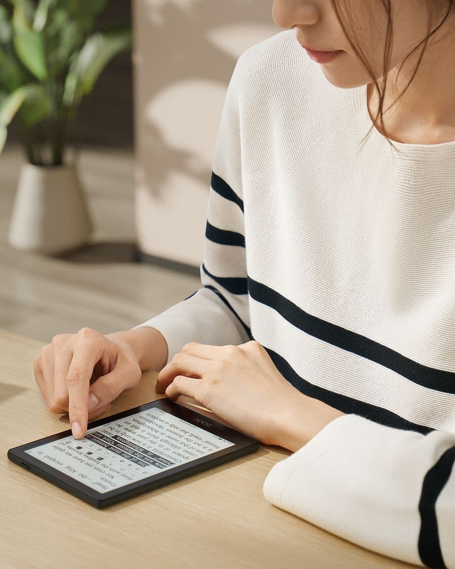 A reader in a striped sweater turning a page on a BOOX Go 6 at a wooden table