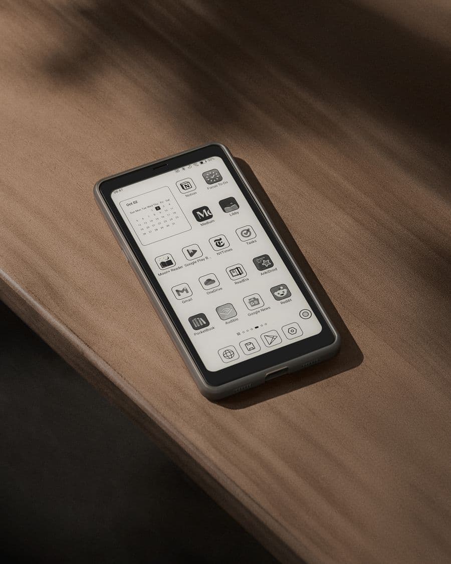 Un BOOX Palma 2 dans un étui gris sur une table en bois, écran d'accueil avec les applications de lecture