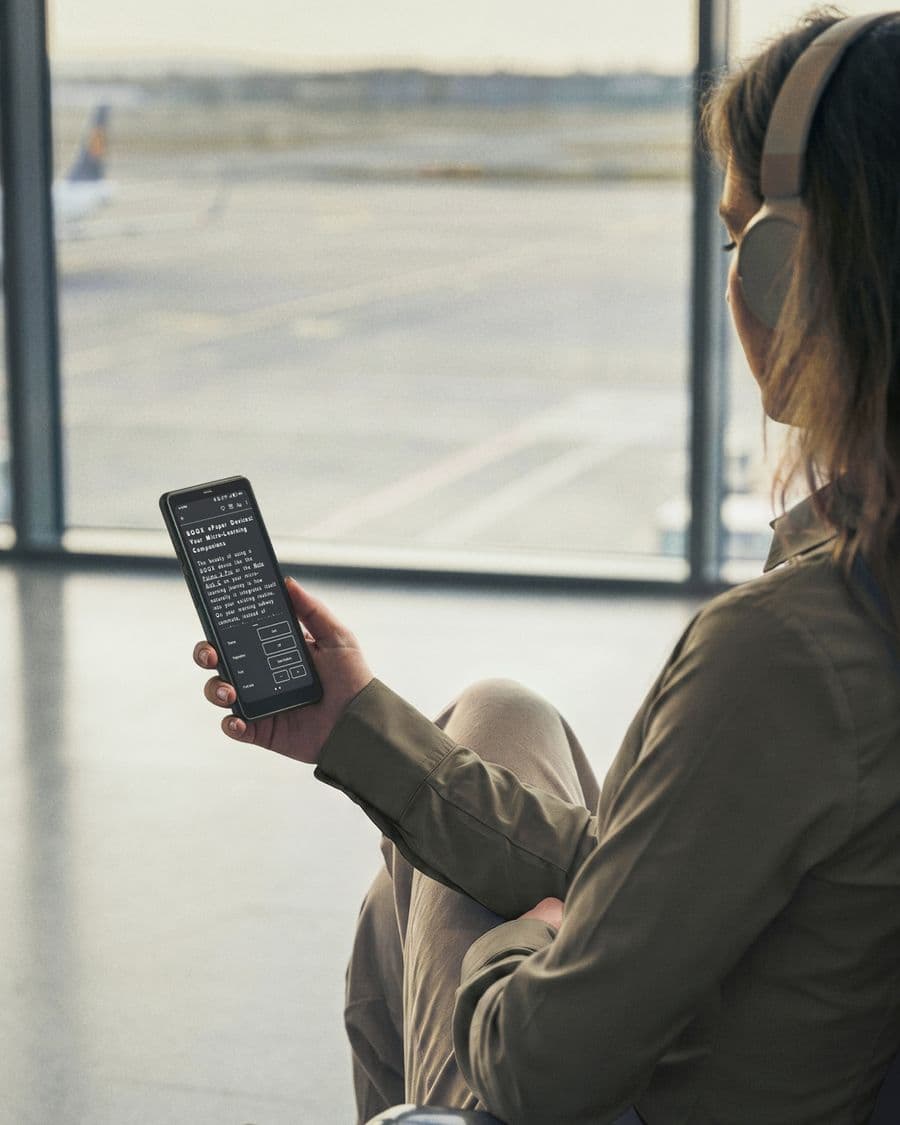 Une voyageuse lit sur un BOOX Palma 2 Pro à une porte d'embarquement, casque sur les oreilles